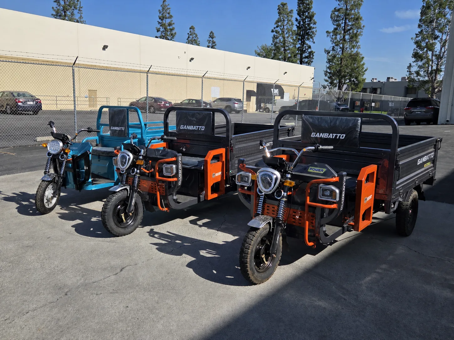 Three Ganbatto electric cargo tricycles lined up outside a commercial facility