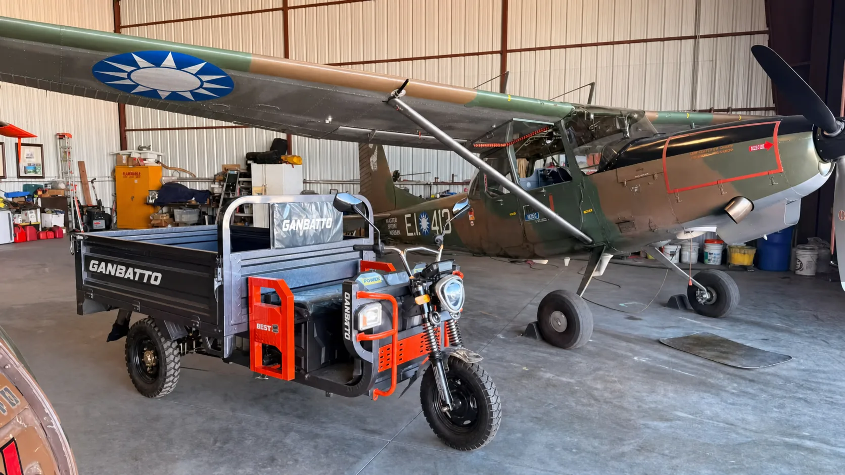 Ganbatto cargo tricycle displayed beside a vintage aircraft in a hangar