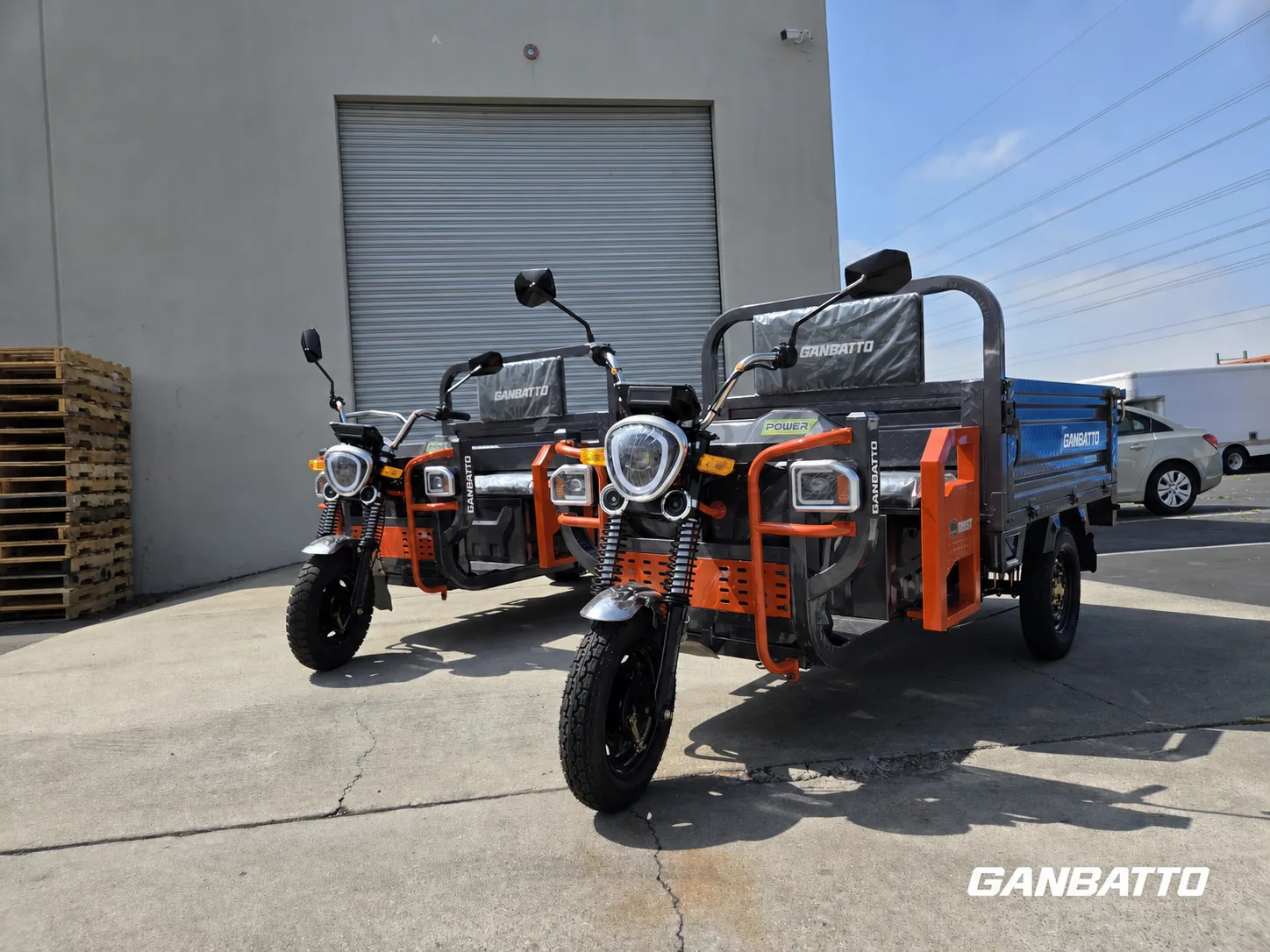Two orange Ganbatto electric cargo tricycles outside a warehouse